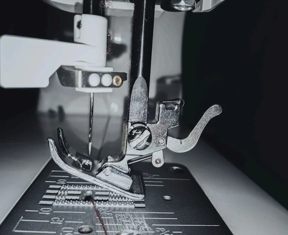 Close-up of a sewing machine needle, presser foot, and feed dogs.