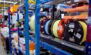 Shelves of colorful 3D printer filament spools in a manufacturing facility.